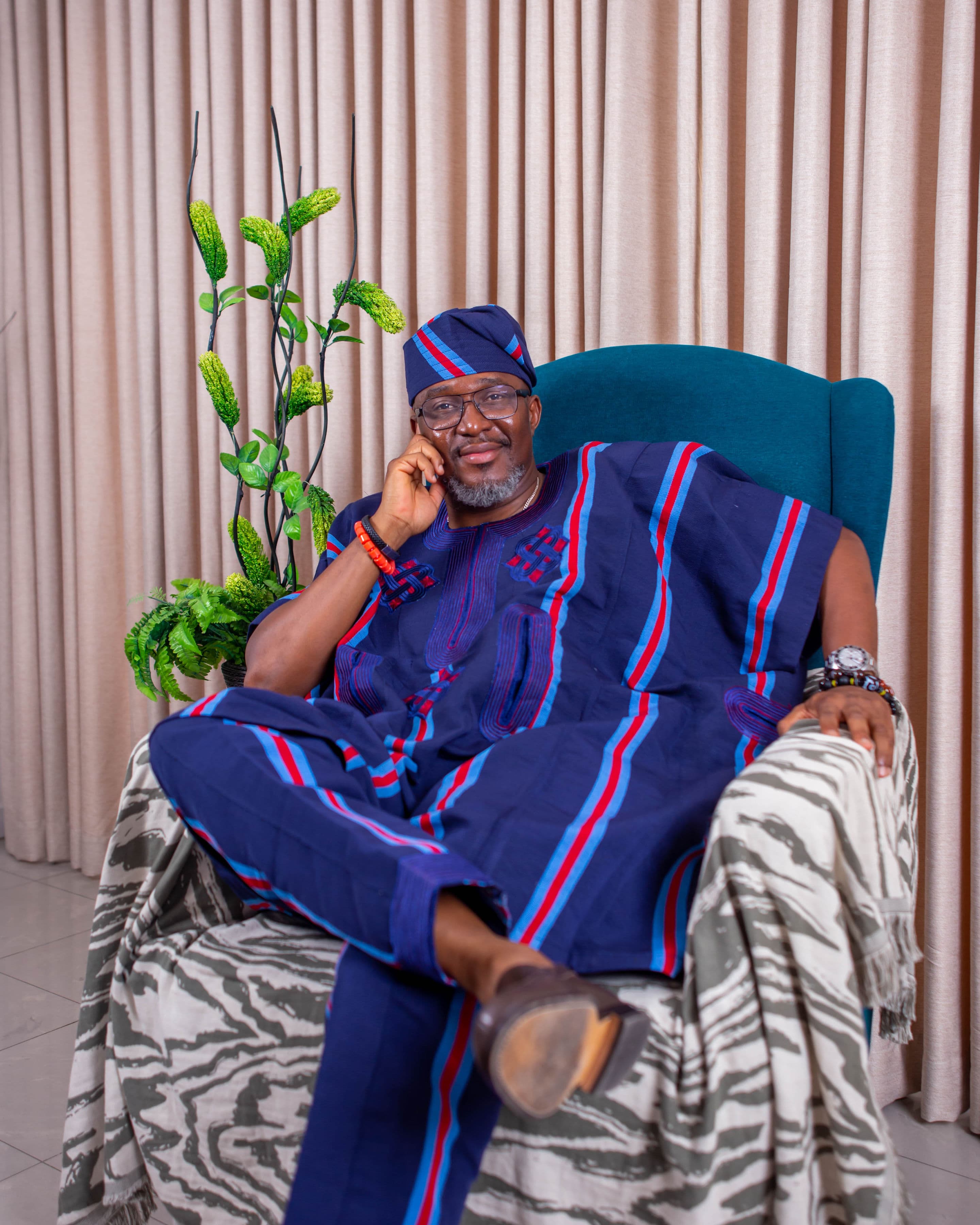 Man in navy agbada lounging in a blue armchair, on the phone